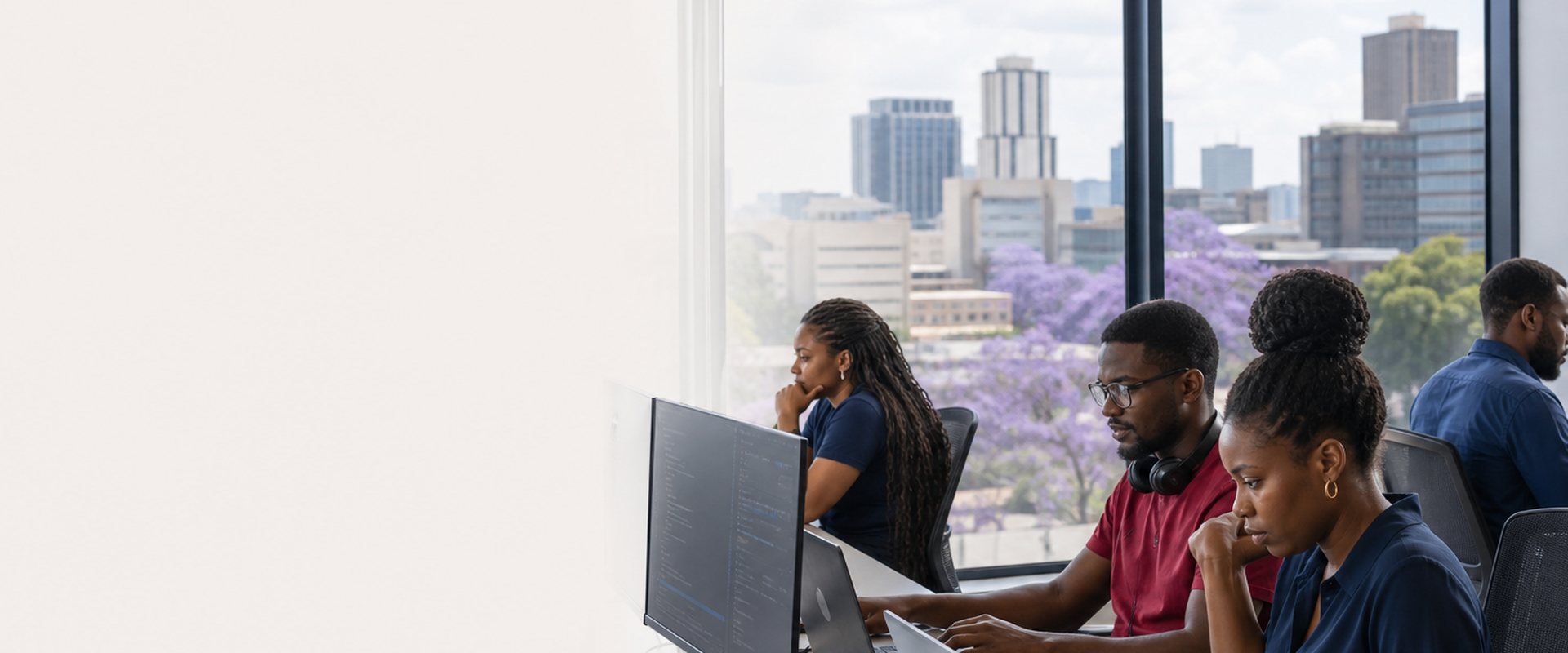 Software developers working in a Harare office with the city skyline behind them